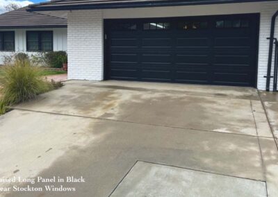 Ranch-style home with sleek black garage doors, Stockton windows, white brick exterior, and ornamental grasses.