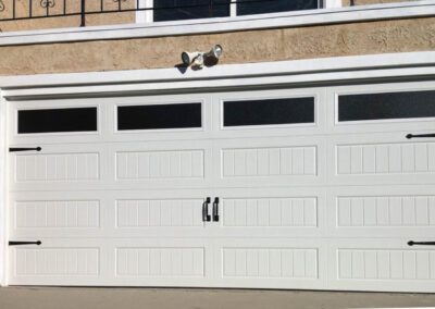 Classic white sectional garage door featuring decorative hardware, windows, and carriage house panel design.