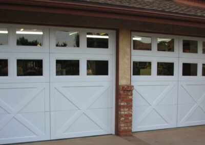 Modern farmhouse with white carriage-style garage doors, crossbuck design, dual windows, and brick column accent.