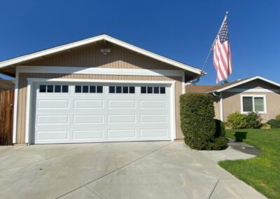 Modern tan house with pristine white garage door & American flag.