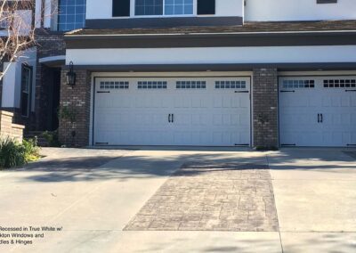 Elegant white Amarr Hillcrest garage doors with decorative windows and hardware frame this modern home's entrance.